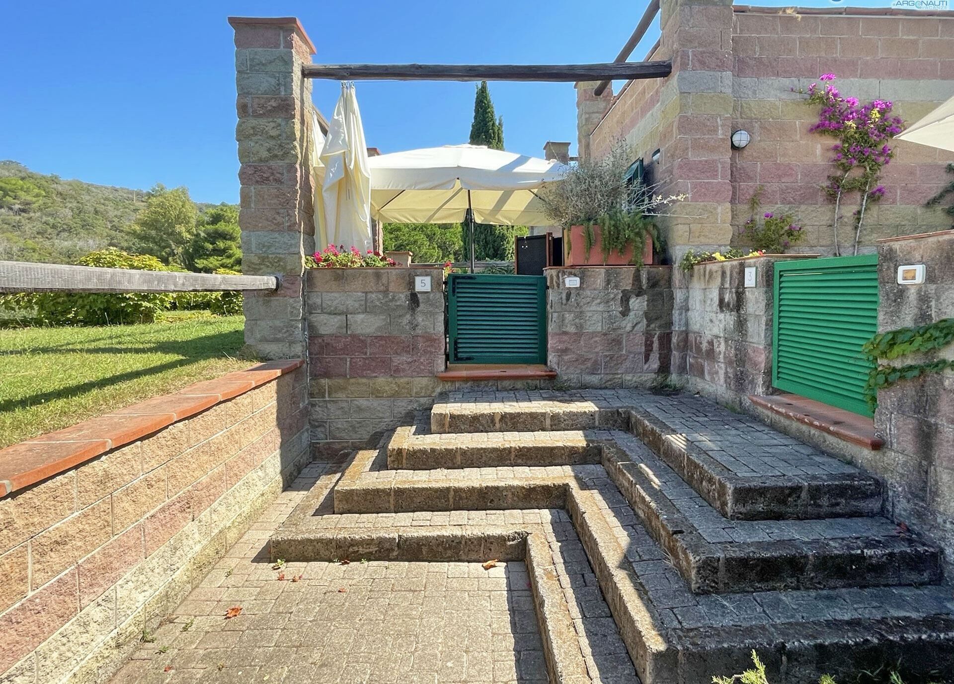Una scala in pietra conduce a un ingresso coperto, con un pannello verde e un ombrello bianco.