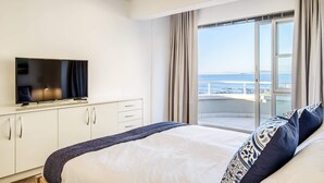 A hotel room with a bed, a TV on a cabinet, and a balcony with a view of the sea.