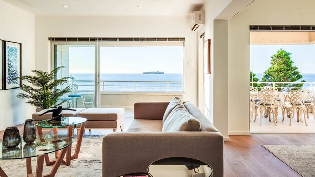 A modern living room with a large sliding glass door leading to a balcony with a view of the sea.