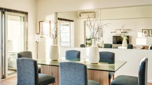 A modern dining area with a glass table and blue chairs, surrounded by white vases and a large mirror.