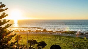A coastal park with a walking path, grassy areas, and a view of the ocean at sunset.
