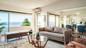 A modern living room with a sofa, a glass coffee table, and a view of the ocean.