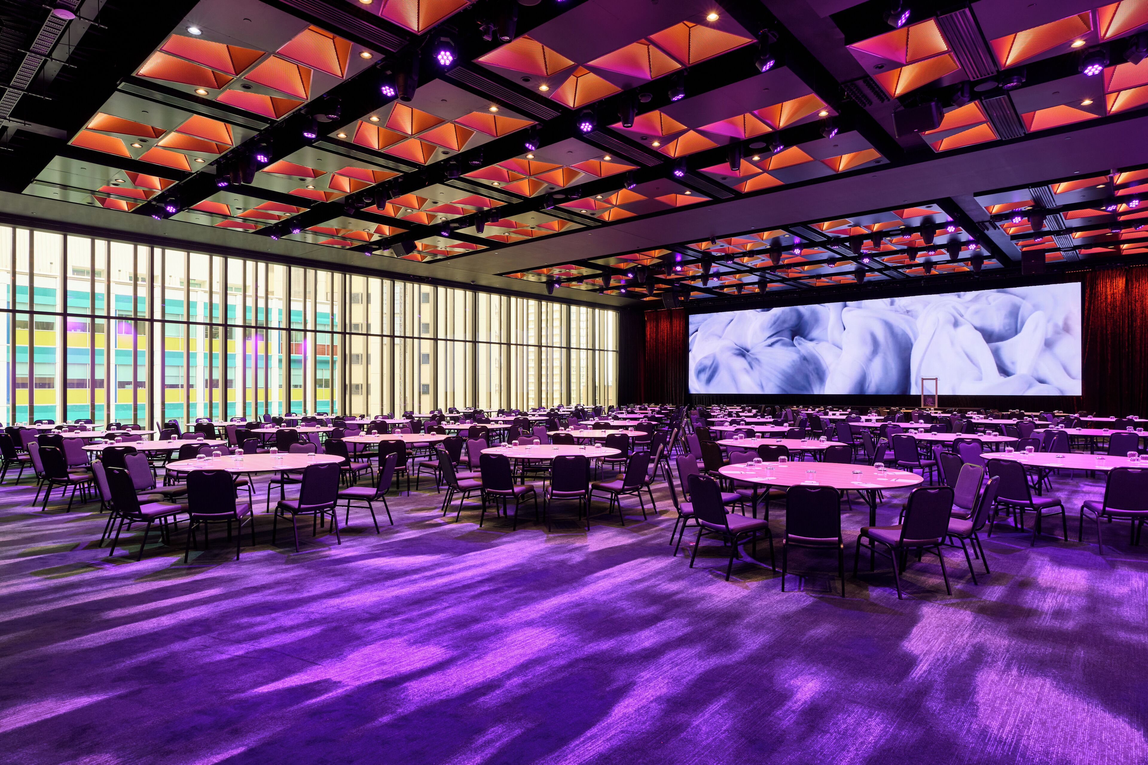 A conference room with round tables, chairs, and a large screen.