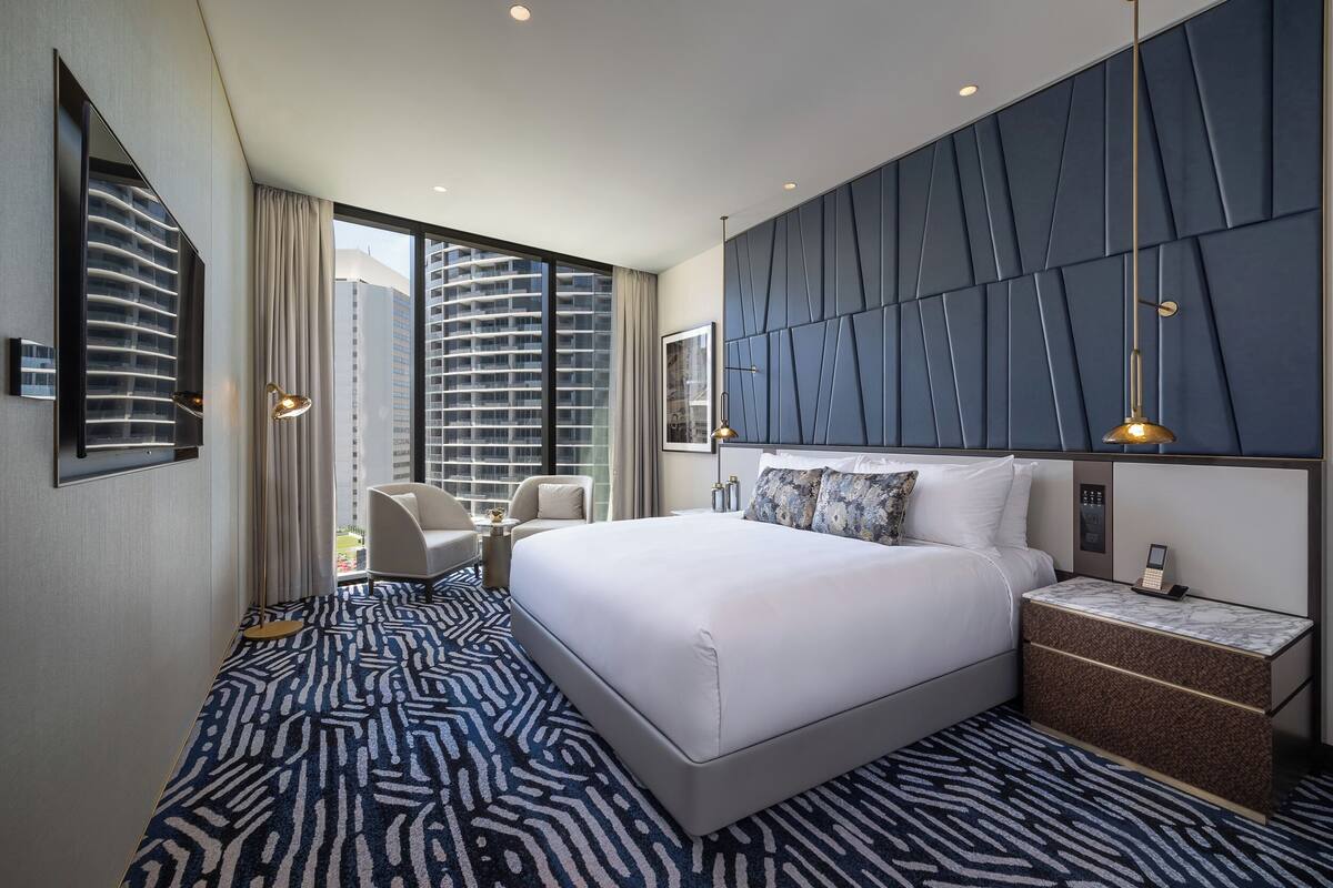 Ein modernes Hotelzimmer mit einem großen Bett, einer Sitzecke, einem Nachttisch und Blick auf hohe Gebäude.