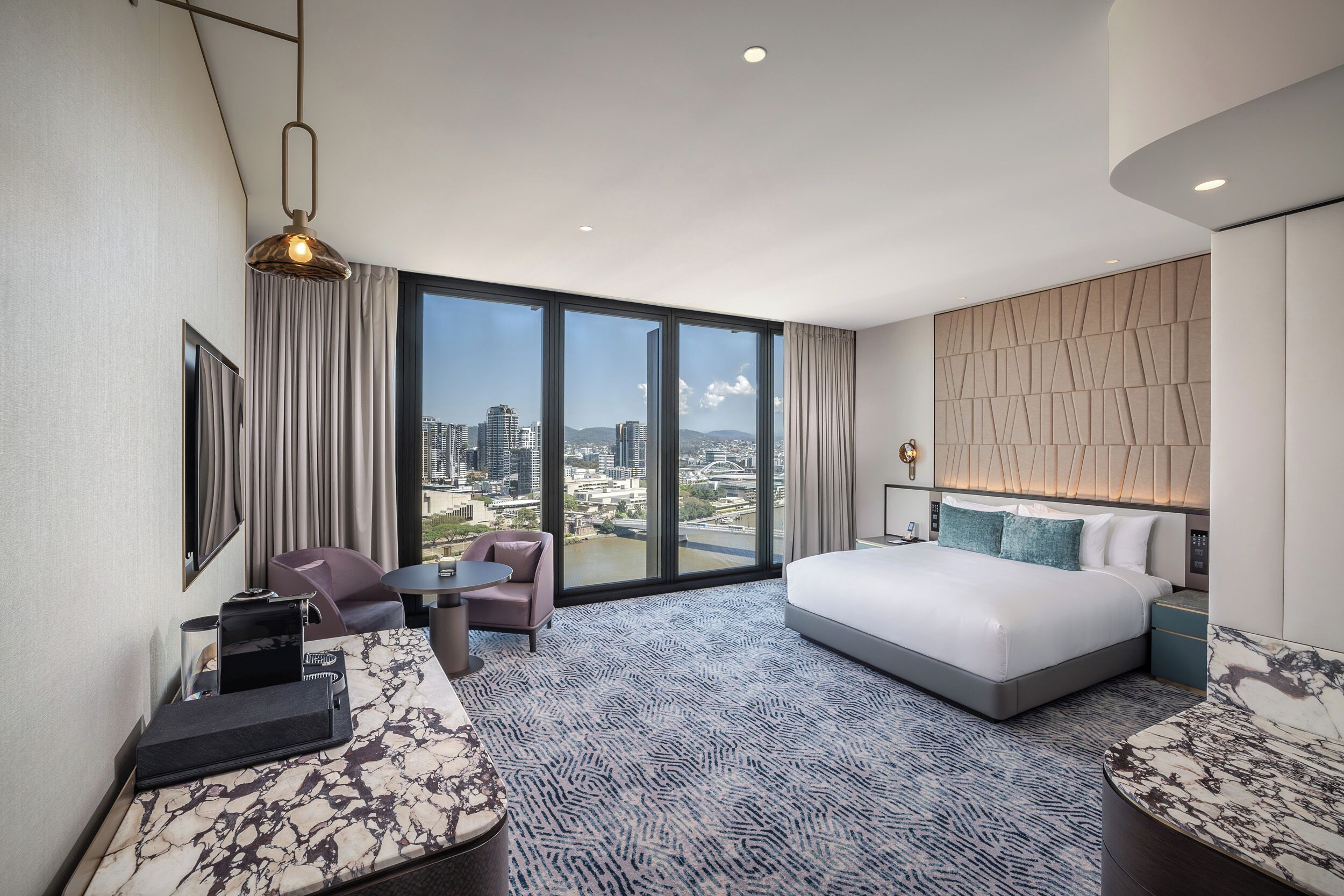 Habitación de hotel con una cama grande, zona de estar, escritorio y vistas a la ciudad.