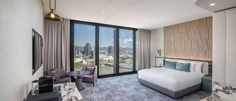 Habitación de hotel con una cama grande, zona de estar, escritorio y vistas a la ciudad.