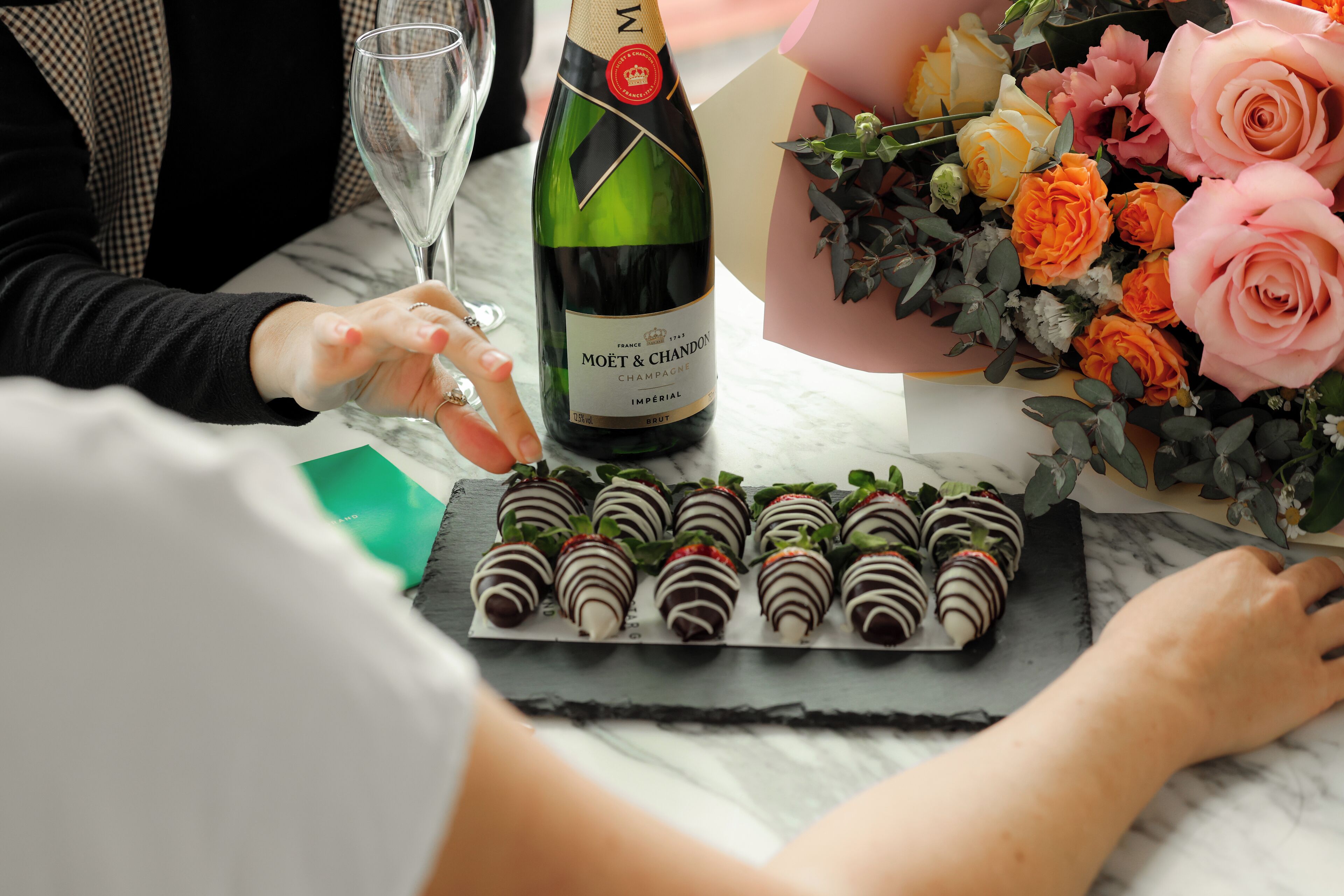 Una botella de Moët & Chandon, un ramo de rosas y fresas cubiertas de chocolate sobre una mesa de mármol.