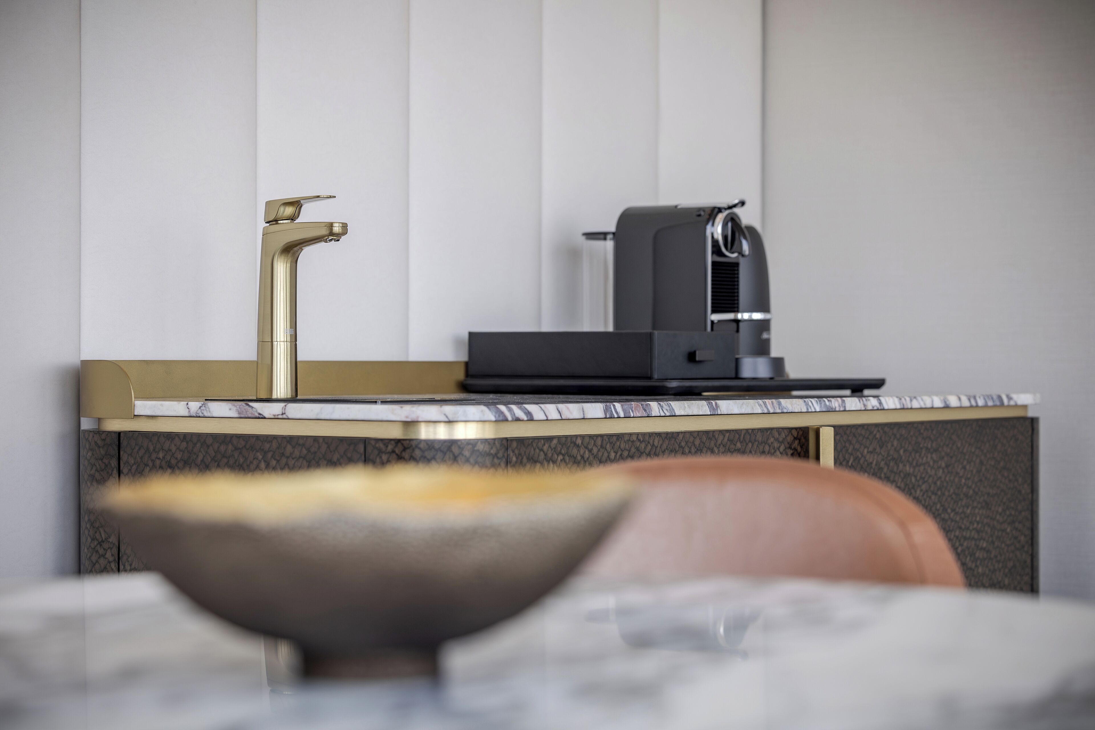 A modern kitchen with a gold faucet, a coffee machine, and a marble countertop.