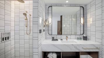 A modern bathroom with a large mirror, a shower with a gold showerhead, and a marble sink.