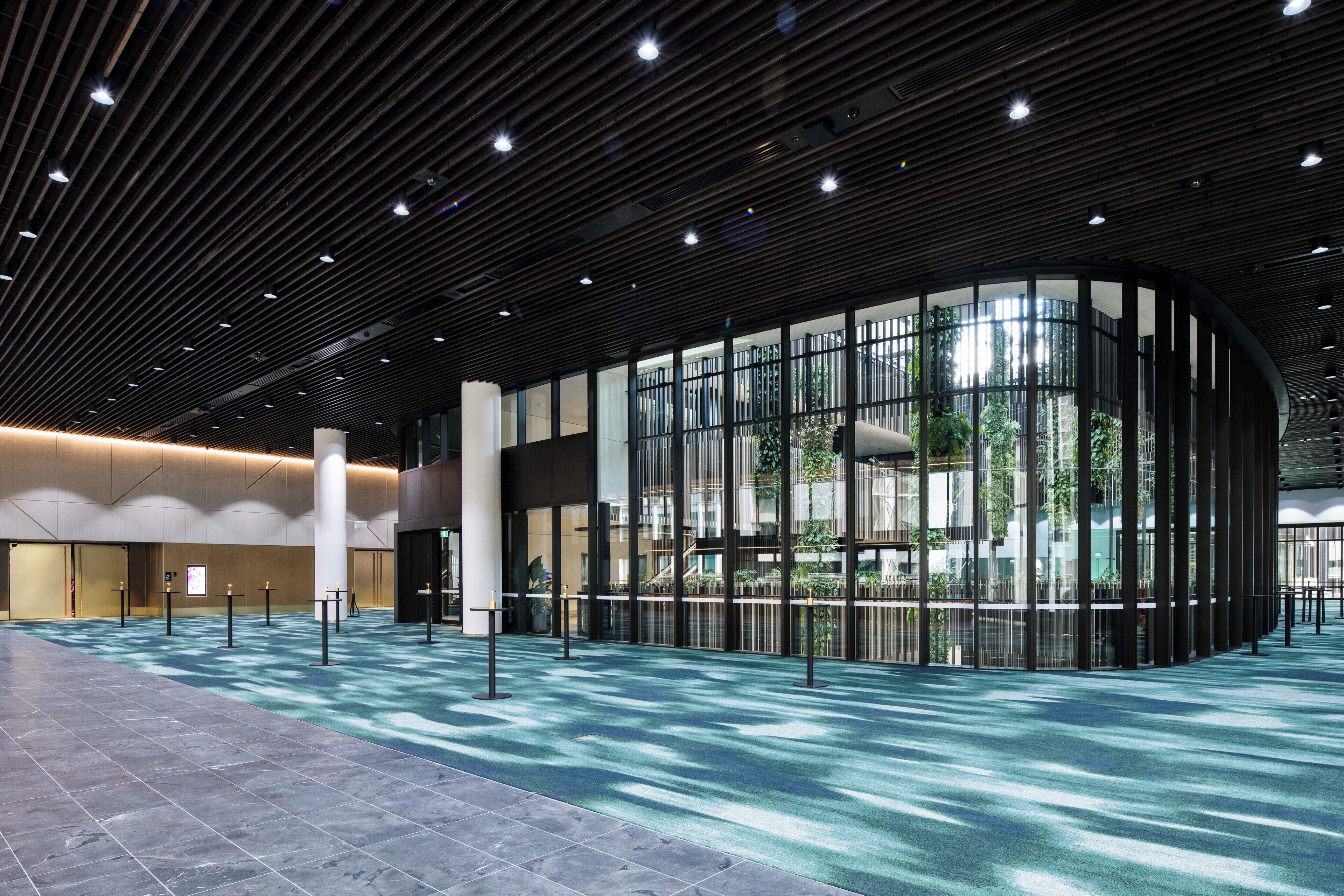 A spacious lobby with a modern design, featuring a curved glass wall, a tiled floor, and a ceiling with linear lighting fixtures.