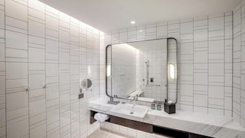 A modern bathroom with white tiled walls, a large mirror, a marble countertop, and a built-in sink.