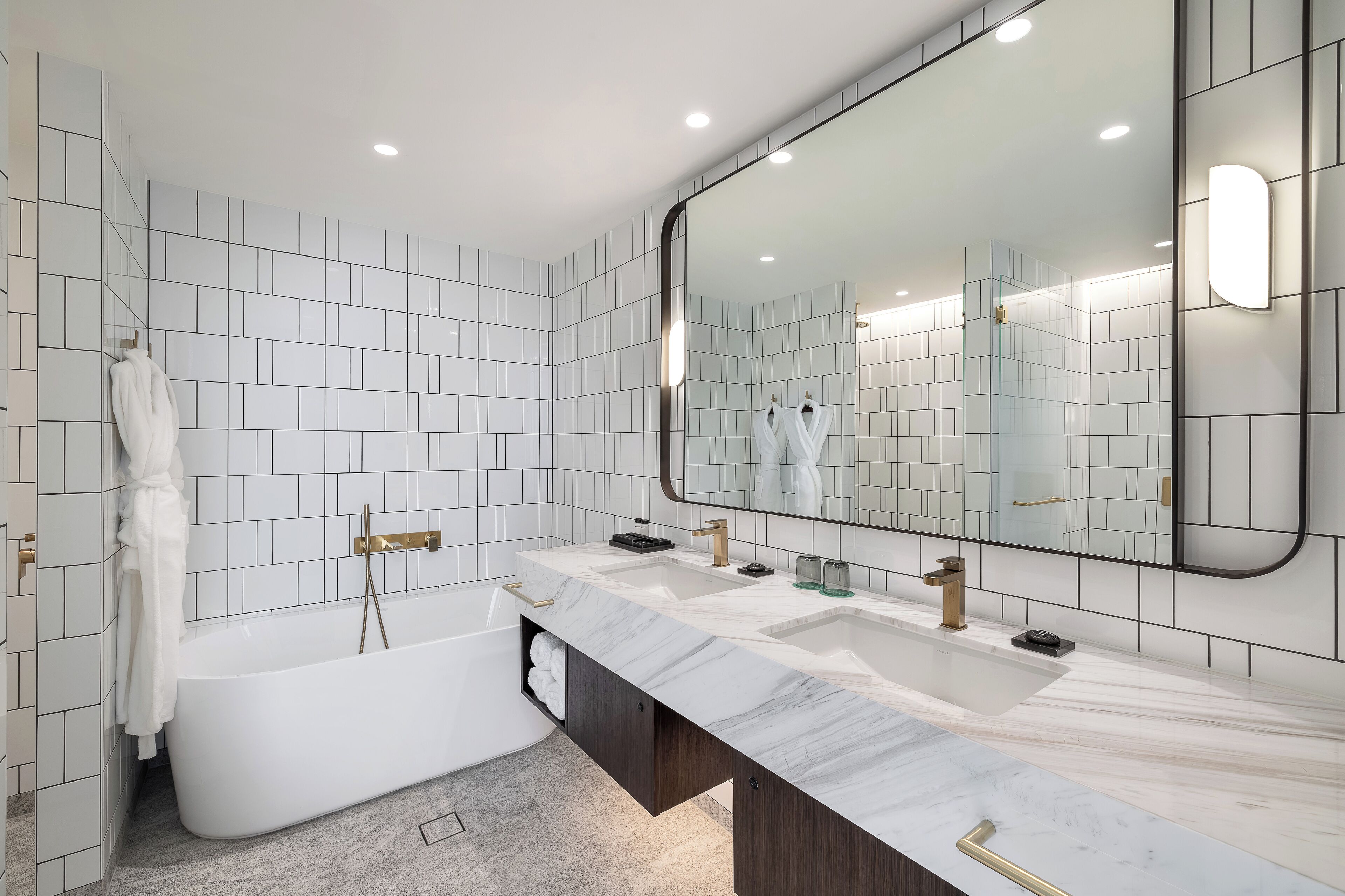 A modern bathroom with a freestanding bathtub, a large mirror, and a marble countertop with dual sinks.