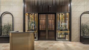 A hotel entrance with a modern design, featuring a reception desk, a glass door with a metal frame, and a tiled floor.