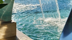 Un élément décoratif aquatique composé d’une structure métallique incurvée, d’un bassin et, en arrière-plan, d’une vue sur la ville.