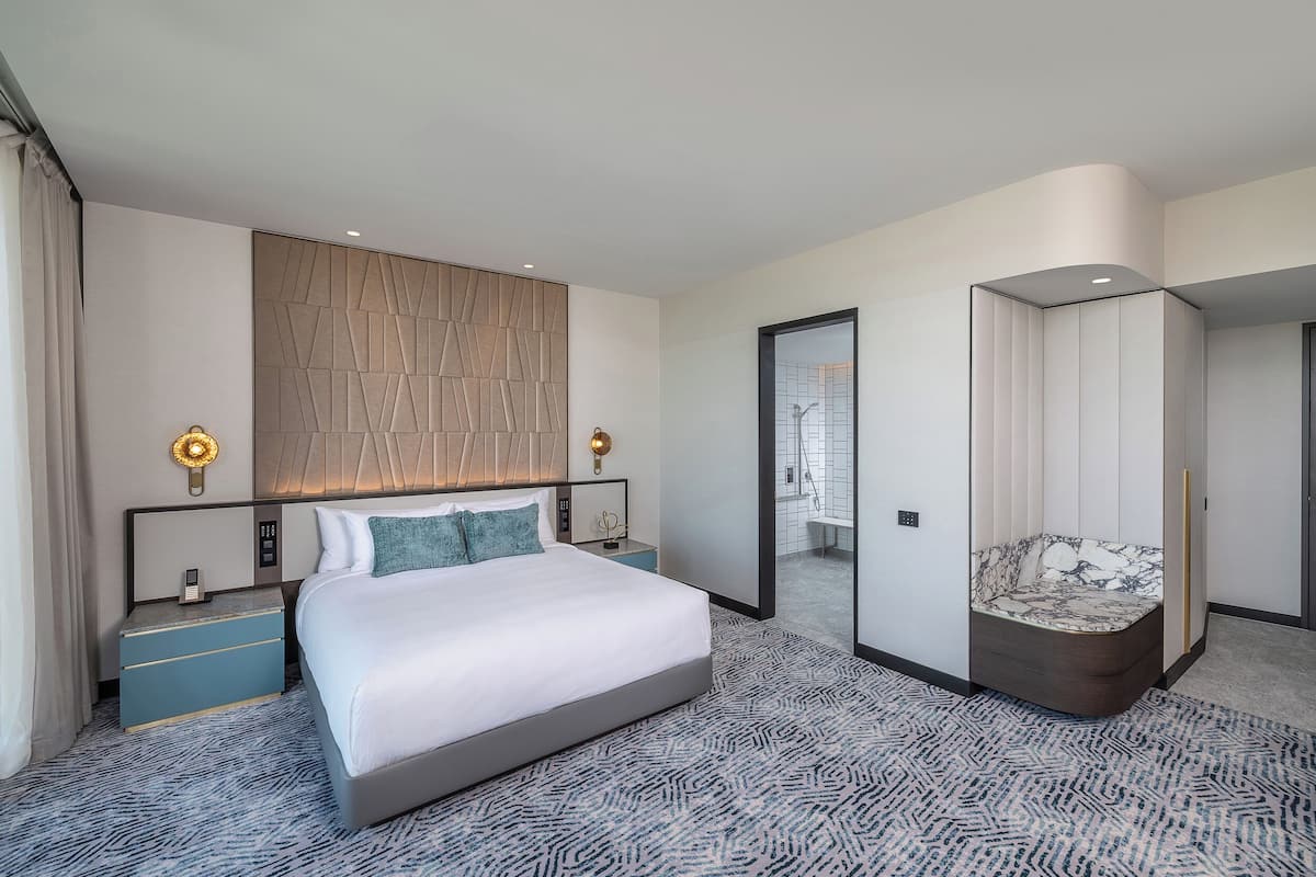 Ein modernes Hotelzimmer mit einem großen Bett, einem Nachttisch, einem Spiegel und einer Sitzecke mit gepolstertem Sitz.