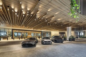 Un hall d’hôtel moderne avec un comptoir d’accueil, trois voitures de luxe et un design de plafond unique.
