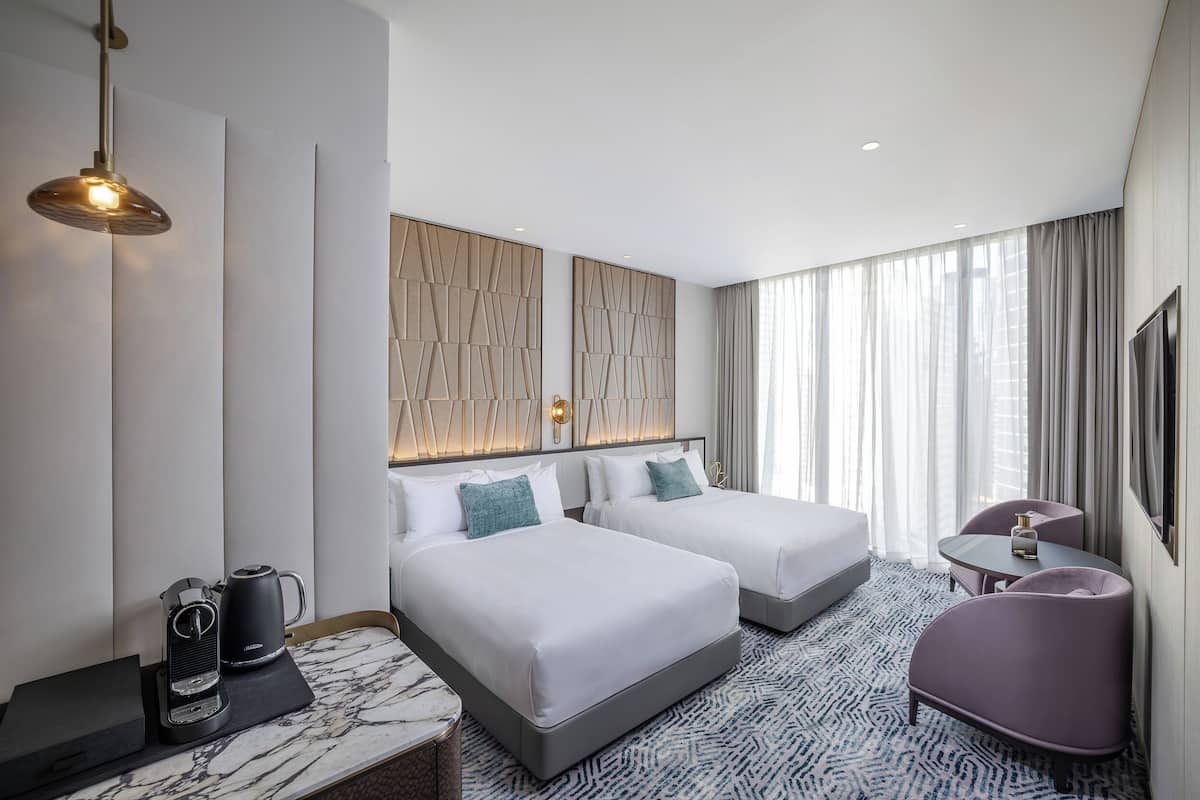 Ein Hotelzimmer mit zwei Betten, einem Schreibtisch, einem Stuhl, einer Kaffeemaschine und einem Fernseher.
