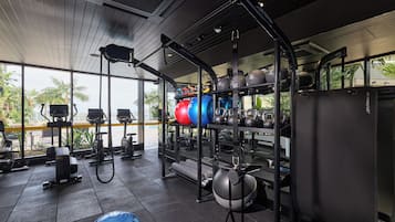 Uma academia com equipamentos de ginástica, suporte para levantamento de peso e uma grande janela com vista para palmeiras.