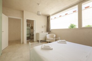 Relax in this serene hotel room featuring a large bed, a comfortable chair, and a shower area.