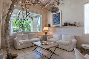 Un salon avec deux canapés blancs, une table basse, une lampe et un arbre décoratif.