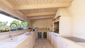 Cocina con vigas de madera, un lavamanos, una alacena para vinos y vistas al exterior con vegetación.