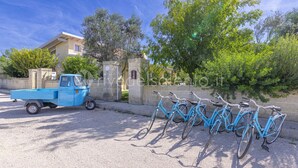 Un camión azul estacionado en un camino de grava, con una fila de bicicletas azules apoyadas contra una pared.