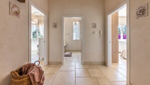 Un corridoio con un cesto di vimini, una porta che dà su una stanza con una finestra e una vista su un balcone fiorito.