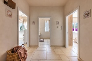 A hallway with a woven basket, a door leading to a room with a window, and a view of a balcony with flowers.