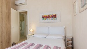 A bedroom with a bed, a nightstand, a lamp, a wall-mounted painting, and a door leading to another room. - Exclusive Villa Reginella with pool in Lecce (Lecce)