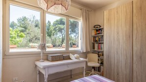 Una camera da letto con un'ampia finestra, un comodino con una lampada, una sedia, una libreria e un letto con copriletto a righe.