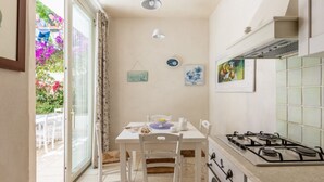 Una cucina con un fornello a gas, un tavolo da pranzo con sedie e vista all'esterno tramite una porta vetrata.