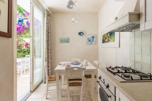 A kitchen with a gas stove, a dining table with chairs, and a view of the outside through a glass door.