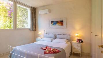Una camera da letto con un letto, due comodini, una finestra con tende, un condizionatore d'aria e un quadro appeso al muro.
