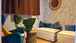 A cozy living room with a blue armchair, a round table with a plant, and two white sofas with blue cushions.