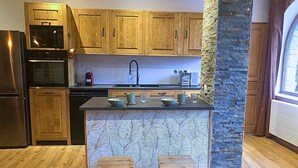 A kitchen with wooden cabinets, a stone accent wall, a built-in island with stools, and a stainless steel refrigerator.
