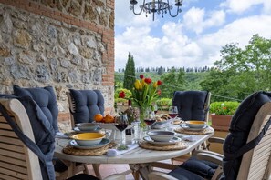 A table set for dining with chairs, a chandelier, and a view of greenery.