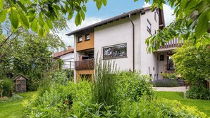 Ein zweistöckiges Haus mit Balkon, umgeben von üppiger Vegetation und einem gepflegten Garten.