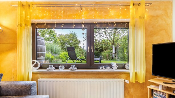 Ein Zimmer mit Fenster, Heizkörper, Stuhl, Fernseher und einem Regal mit Büchern und Dekoration.