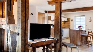 Ein rustikales Interieur mit freiliegenden Holzbalken, einem Fernseher auf einem Holzständer und einer Küche im Hintergrund.