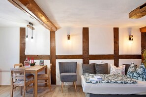 A room with a wooden table, a grey chair, a bed with patterned bedding, and exposed wooden beams.