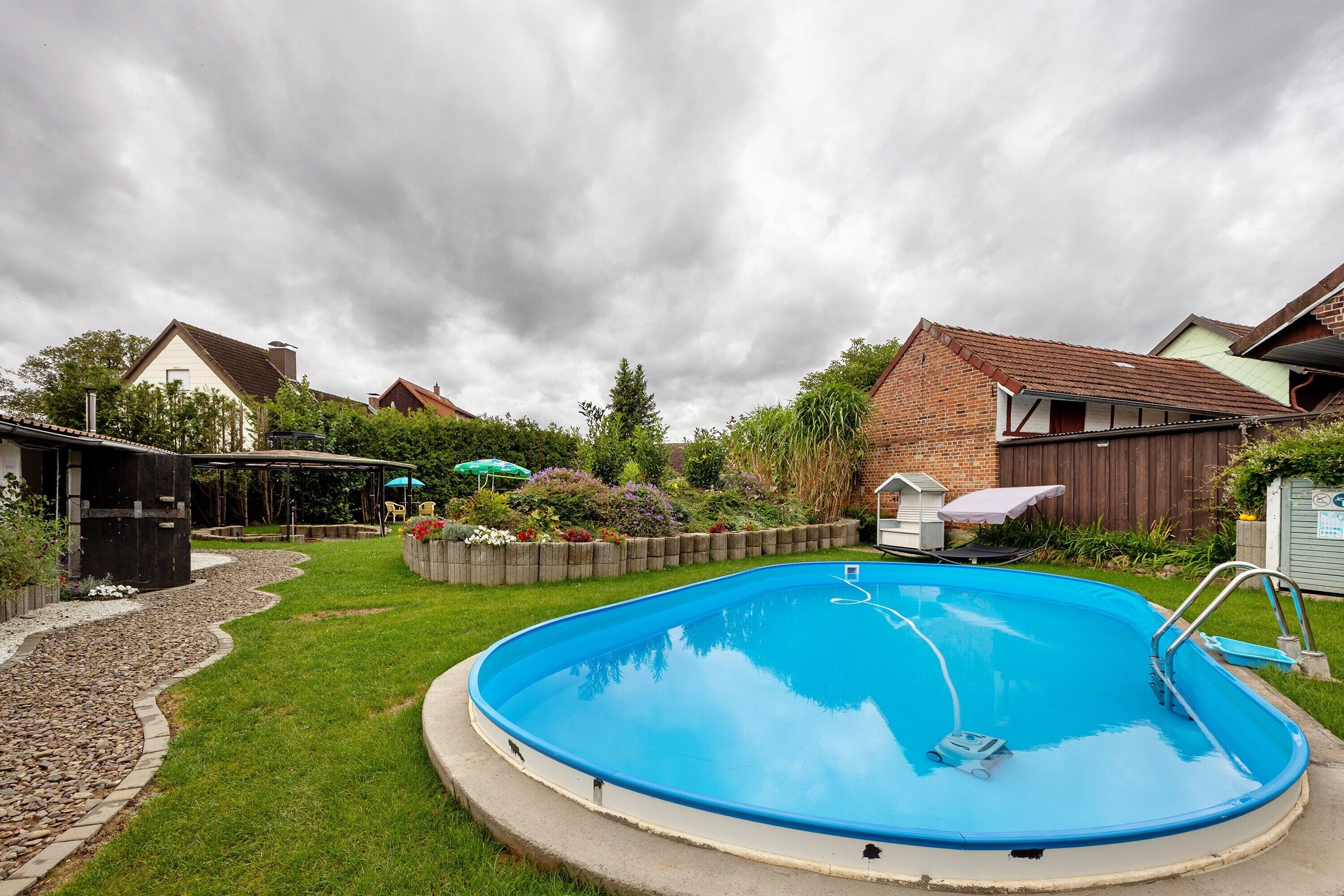 A residential backyard with a swimming pool, a patio area, and a garden.