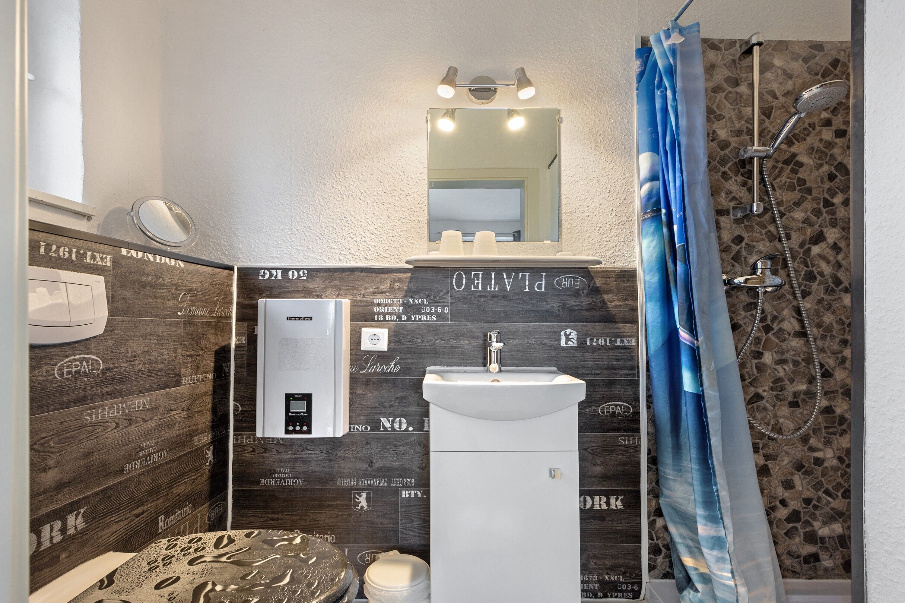 A bathroom with a wooden wall, a sink, a mirror, a shower, and a towel rack.