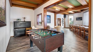 A room with a foosball table, a piano, and a dining area with chairs and a table.