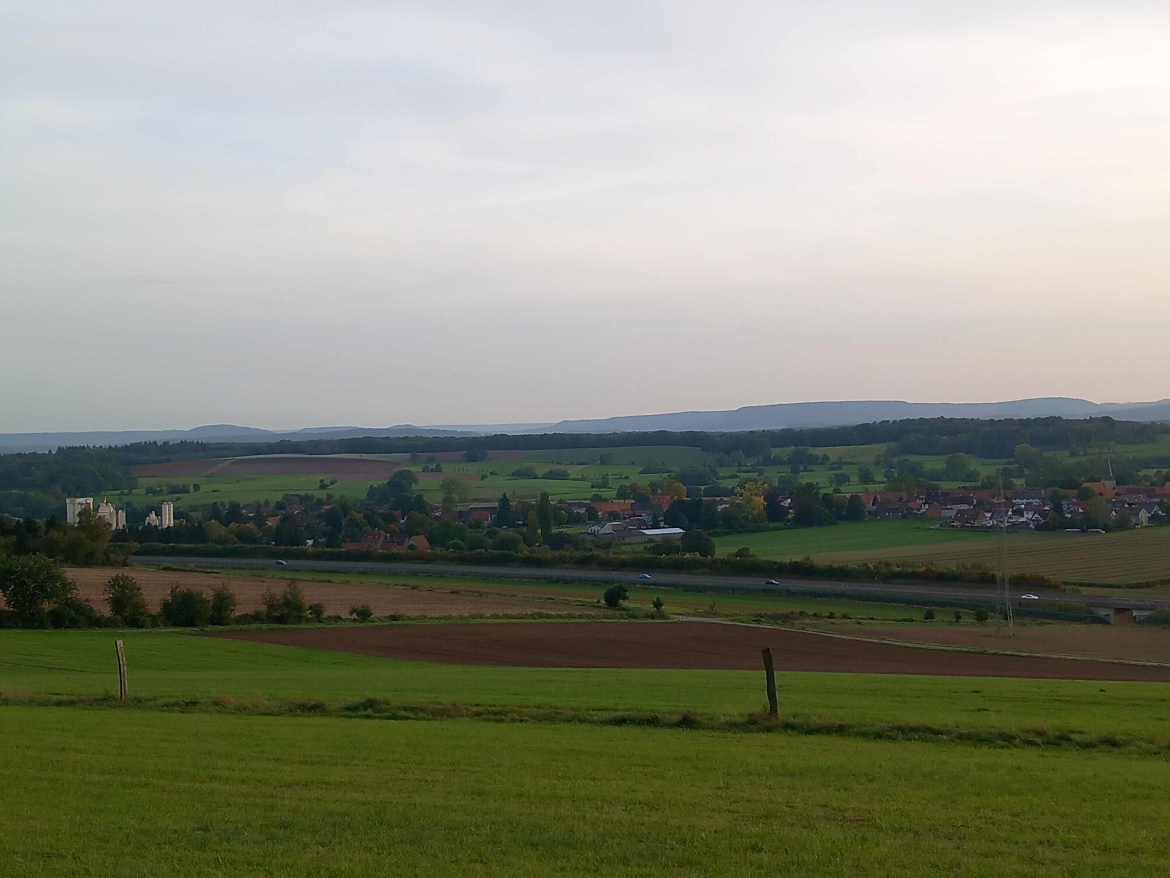 Ländliche Landschaft mit Feldern, einem Fluss und fernen Hügeln.
