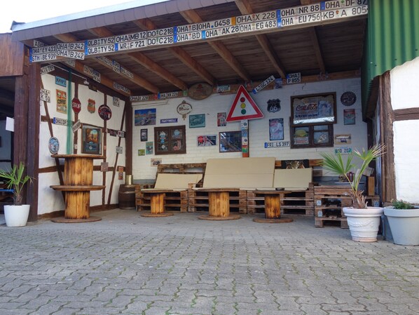 Un espacio de estar al aire libre con encanto, con mesas y bancos de madera, rodeado de plantas en macetas y diversas decoraciones murales.