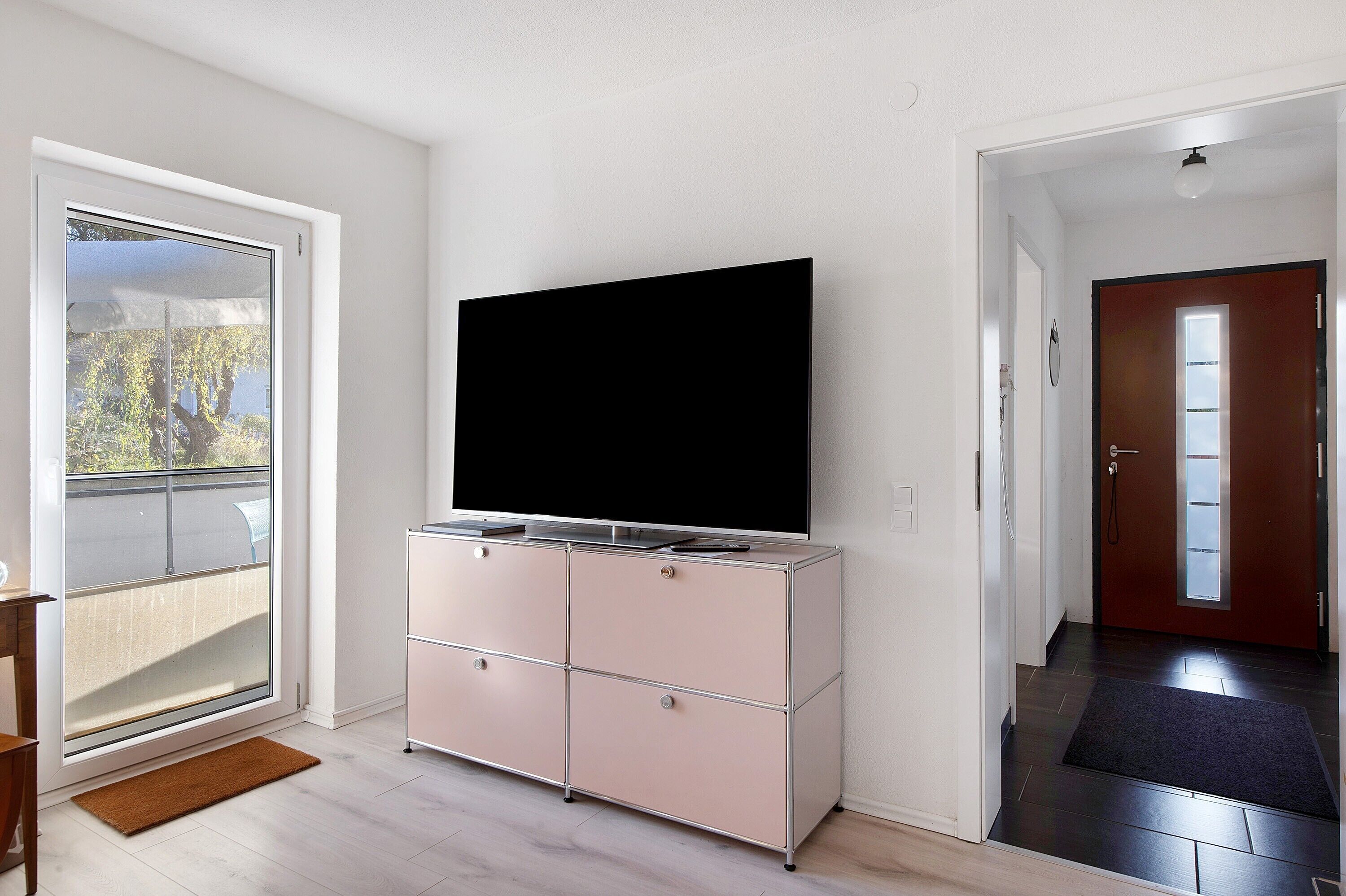 A room with a sliding glass door, a pink cabinet with a flat-screen TV, and a wooden floor.