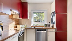 Une cuisine moderne dotée d’appareils électroménagers en acier inoxydable, d’une fenêtre offrant une belle vue et de meubles de rangement rouges.