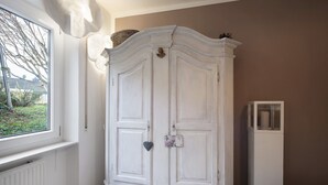 Une armoire blanche surmontée d’un panier, un petit objet décoratif sur la porte, et une haute armoire à vitrine.