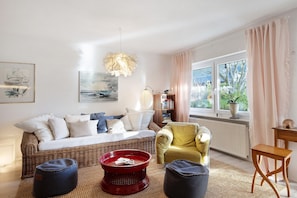 Una sala de estar acogedora con un sofá de mimbre, un sillón amarillo, una mesa de centro roja y una estantería.