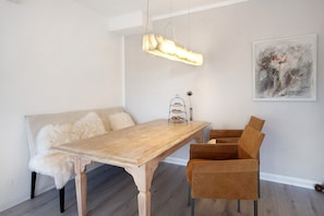 Un comedor con mesa de madera, sofá con cojines mullidos e iluminación colgante.
